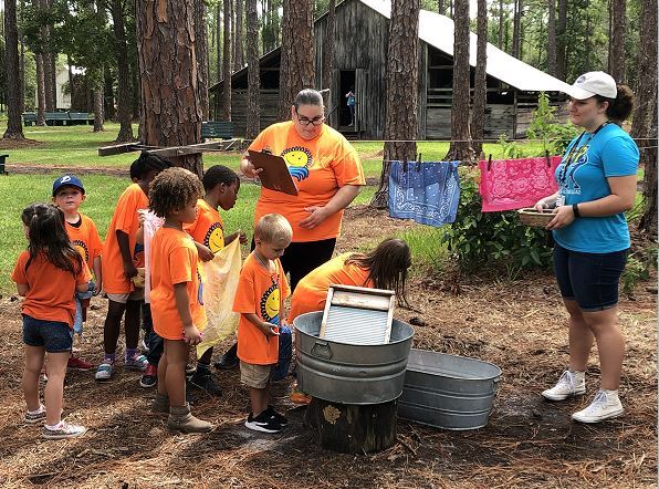 seven youth with 2 camp guides showing them how they used to wash clothes with a washboard