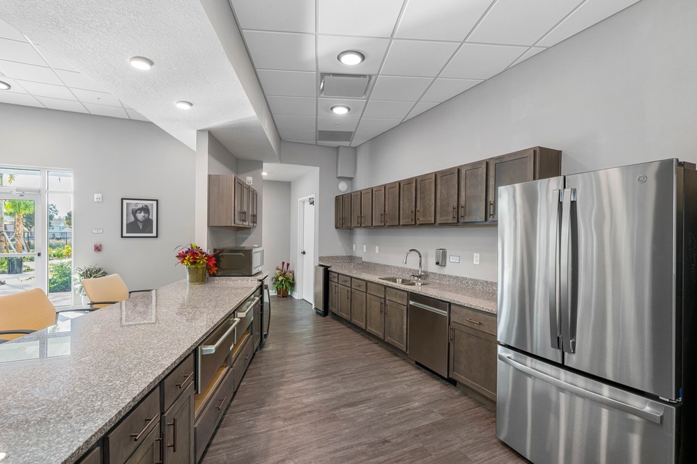 Downstairs community room kitchen with fridge inside The Legacy at Jordan Park senior midrise building.
