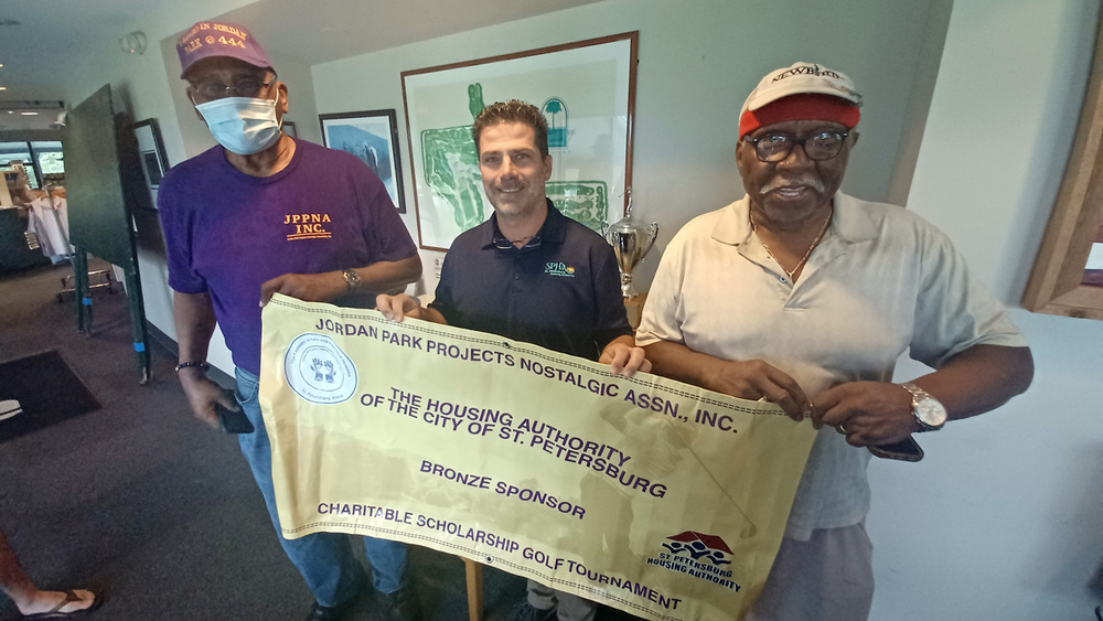 Three men holding a banner for the Jordan Park Scholarship Golf Tournament.