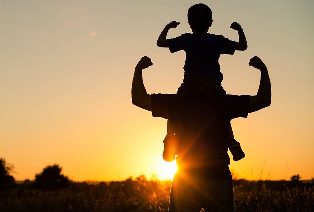 Child sitting on the shoulders of an adult looking at a sunset