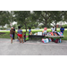 Backpacks and snacks on tables with green grass and people standing in front of the tables.