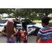 Policeman giving a tour of his police car to children and parents with a child holding an orange drink.