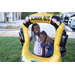 Two girls standing behind a balloon school bus with cars parked in the background.