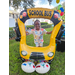 Child smiling while standing behind a balloon yellow school bus at Disston Place Apartments.