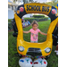 Child wearing pink shirt with butterfly smiling and standing behind balloon school bus at Disston Place Apartments Back to School Event 2023.
