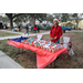 Person in red shirt and red hat standing by table with at Very Merry Holiday Party in Jordan Park.